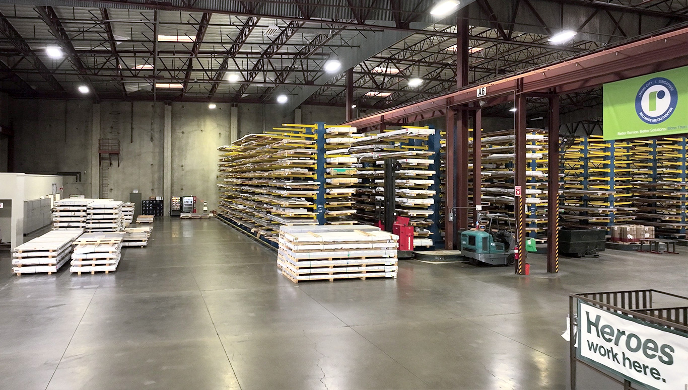 Warehouse of steel and aluminum products on racks is shown with corporate banners hanging up.