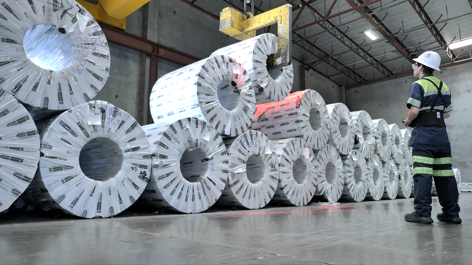 One wrapped steel coil among many is being lifted up by a machine